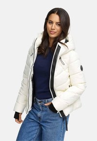 Veste blanche rembourrée avec une capuche amovible, des accents noirs, des poches zippées et des poignets élastiques, assortie à un haut sombre et un jean bleu.
