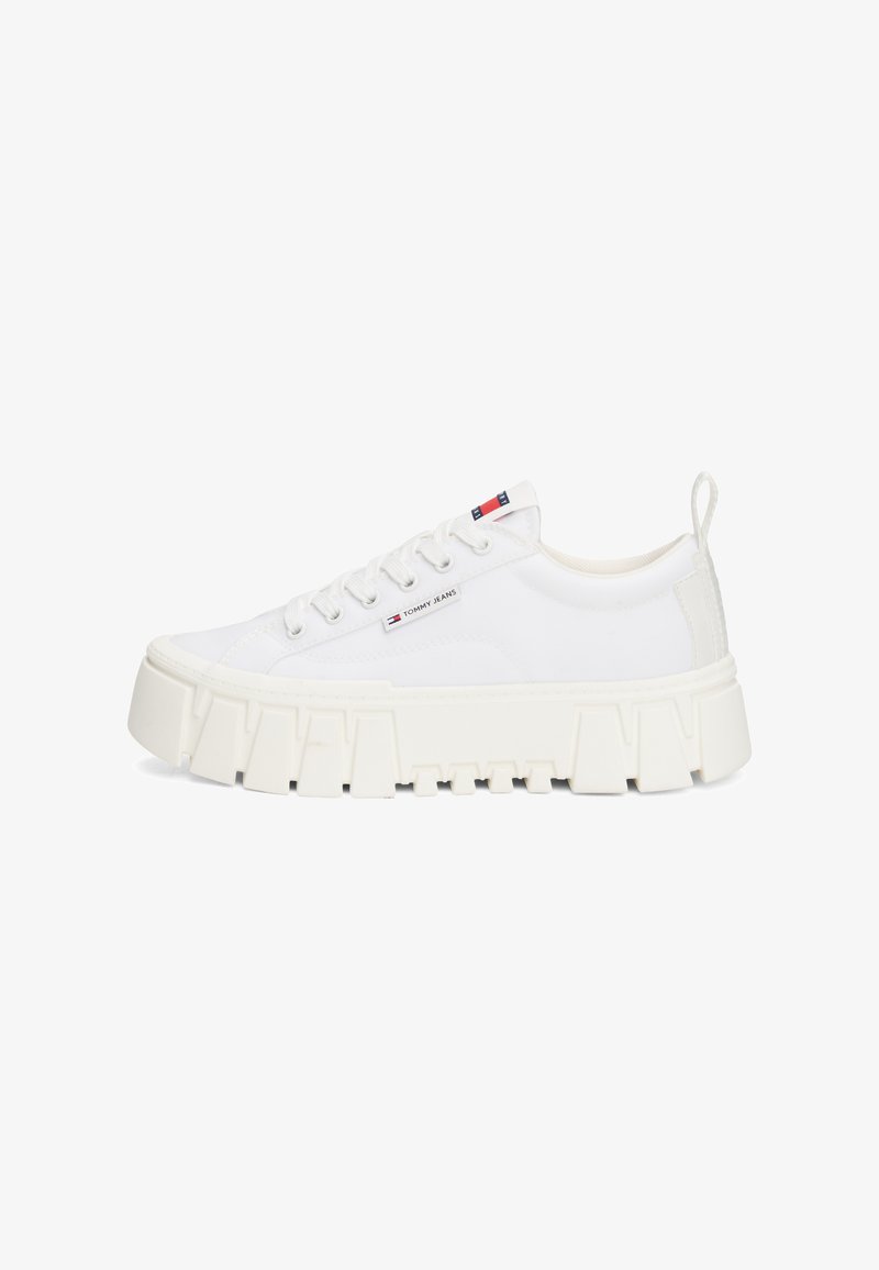 White platform sneakers with a textured rubber sole, flat laces, and a small logo tag on the side. Smooth synthetic upper, rounded toe.