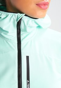 Chaqueta de color verde menta con cremallera, capucha fruncida, cremallera negra y acentos de logo. Fabricada con un tejido suave y ligero.