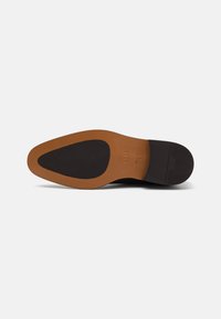Suola di scarpa in pelle nera con una porzione di gomma marrone. Presenta un tacco rialzato, una texture liscia e un'impronta del logo sfumata sulla suola.