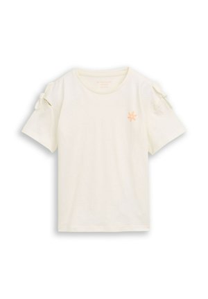 T-shirt crème à manches courtes avec col rond, petite fleur orange sur la poitrine et nœuds attachés à chaque manche.