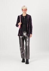 Blazer noir à sequins, blouse noire transparente, pantalon argent métallique, sac à main rose et lunettes de soleil rouges, présentant un design élégant et des textures brillantes.