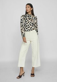 Leopardmönstrad långärmad blus med samlad halsringning, ihopparad med höga, vida krämfärgade byxor och bruna klacksandaler.