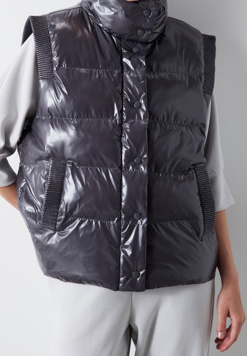 Gepolsterte, dunkelgraue Weste mit glänzender Oberfläche, hohem Kragen, Druckknöpfen und gestrickten Schulterakzenten; verfügt über seitliche Taschen.