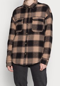 Brun och svart rutigt flanellskjorta med krage, två framfickor och knappstängning. Mjuk текстur, långa ärmar och avslappnad passform.