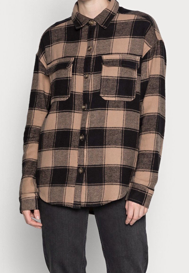 Brun och svart rutigt flanellskjorta med krage, två framfickor och knappstängning. Mjuk текстur, långa ärmar och avslappnad passform.