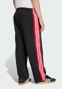 Svarta nättrackbyxor med tre röda och vita vertikala ränder längs ytterkanterna. Elastisk midja och lös passform.