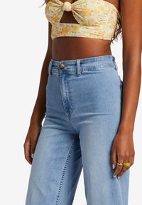 Light blue high-waisted jeans with a classic five-pocket design and a gold button closure. The fabric has a smooth texture and slight fade.