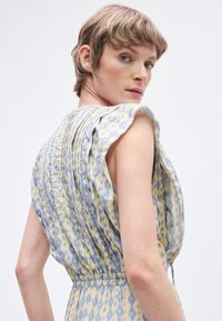 Αέρινο αμάνικο φόρεμα σε κίτρινο και μπλε με λαιμόκοψη με βολάν, περίπλοκα σχέδια και σούρες στη μέση για ρευστή σιλουέτα.