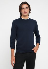 Chemise à manches longues bleu marine avec un col rond, accent blanc en contraste au niveau du col et une texture douce et lisse.
