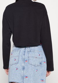 Black cropped long-sleeve shirt paired with a light blue denim skirt, featuring colorful embroidered logo patches and frayed hem.