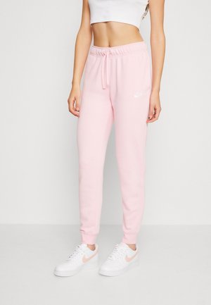 Vrouw draagt lichtroze Nike joggingbroek met een tailleband met trekkoord en witte sneakers met roze swoosh-logo's.