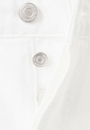 Gros plan d'un tissu en denim blanc avec trois boutons-pression argentés visibles le long d'un détail de couture.