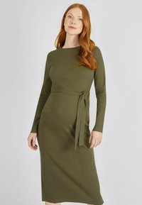 Olivegrünes geripptes Strickkleid mit langen Ärmeln, rundem Ausschnitt und einem Bindegürtel in der Taille. Knielang, figurbetont.