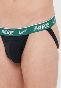 Schwarze Beutelhöschen-Unterwäsche mit einem grünen elastischen Bund, der mit weißem Nike-Branding versehen ist. Der Stoff wirkt glatt und dehnbar.