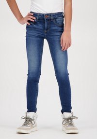 Tmavě modré skinny džíny s uzavřením na knoflík, pětipocket designem a mírným vyblednutím. Stylizované s bílou košilí a šedými vysokými teniskami.
