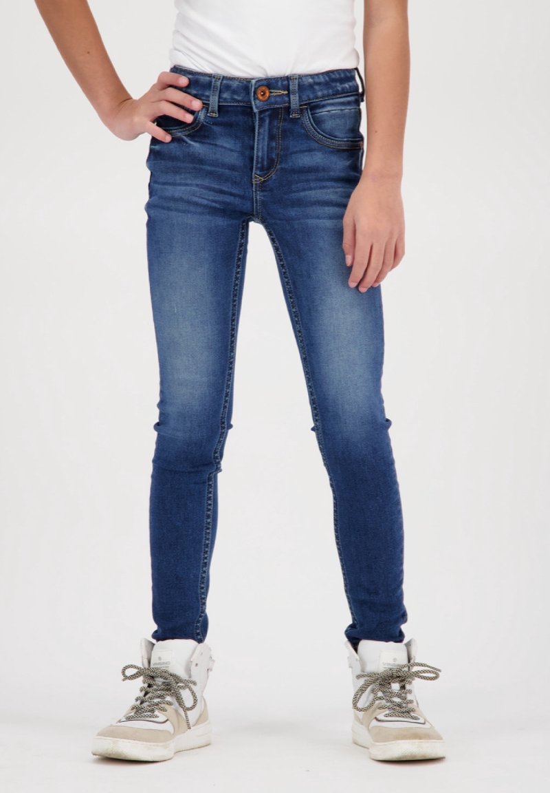 Tmavě modré skinny džíny s uzavřením na knoflík, pětipocket designem a mírným vyblednutím. Stylizované s bílou košilí a šedými vysokými teniskami.
