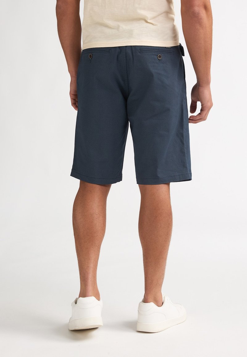 Pantalones cortos azul marino hechos de tela texturizada, con dos bolsillos traseros con botones marrones y un dobladillo que cae justo por encima de las rodillas.