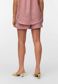 Top suelto de color rosa claro con un dobladillo curvado, combinado con pantalones cortos a juego. La ropa presenta una tela texturizada. Incluidas sandalias amarillas de tacón abierto.
