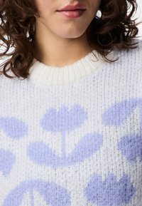 Ljuslila stickad tröja med ett blommönster i mörklila. Kragen är ribbad och har ett mjukt, strukturerat tyg.