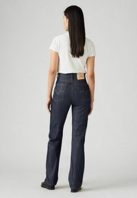 Ciemnoniebieskie dżinsy z wysokim stanem, prostą nogawką i wyraźnymi tylnymi kieszeniami z detalami w stiche. Noszone z dopasowanym białym t-shirtem.