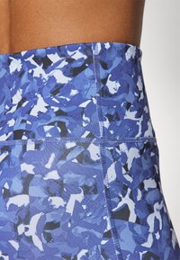 Högmidjade blå leggings med ett texturerat abstrakt mönster i olika nyanser av blått och svart, med synliga sömmar och en jämn yta.