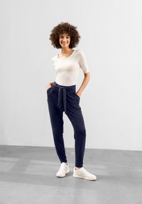 Mörkblå, högmidjade byxor med ett knytbälte, slät textur, kombinerat med en åtsittande krämfärgad topp och vita sneakers.