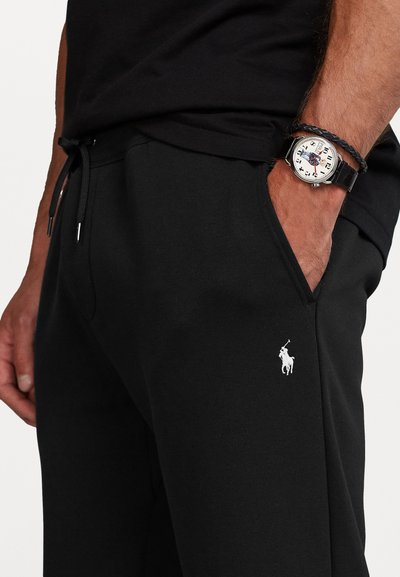 Black cotton sweatpants with side pockets, drawstring waistband, and white logo accent. Smooth texture with a relaxed cut for comfort.