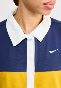 Navy blue and yellow polo shirt with a white collar, featuring a front placket and a small white Nike logo on the chest. Textured fabric.