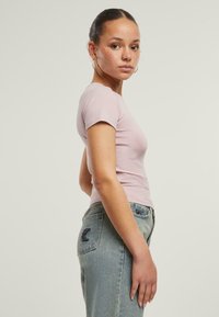Lys rosa tettsittende t-skjorte med korte ermer, paret med lys blå jeans med baklomme-design og minimal slitasje.