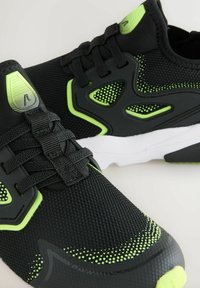Black athletic shoes with mesh upper, green accents, rounded toe, and textured sole. Features laces and perforated detailing.
