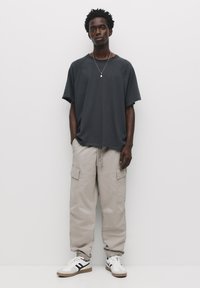 Szary, oversize t-shirt, beżowe spodnie cargo oraz białe sneakersy z czarnymi akcentami. Luźny krój, posiada kieszenie i elastyczne mankiety u spodni.