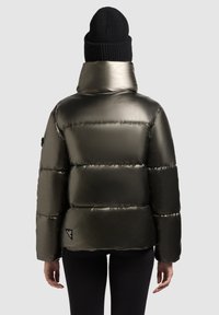 Puffet jakke i metallisk olivengrøn, med høj krave, vandret syninger og logo-lapel på venstre ærme. Sort strikket beanie.