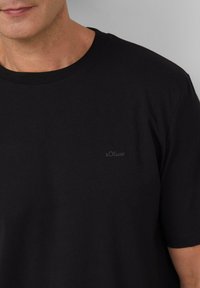 Zwarte katoenen T-shirt met korte mouwen, ronde hals, met een klein, subtiel s.Oliver-logo in donkergrijs op de linkerborst.