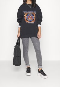 Sudadera negra de gran tamaño con un estampado gráfico colorido y mangas largas blancas, combinada con jeans skinny grises y zapatillas negras.