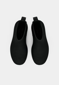 Svarta glidskor i ett slätt gummimaterial, rundad form, minimalistisk design och små handtag vid häl för enkel påtagning.