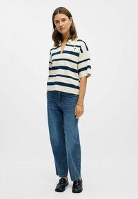 Krämfärgad och marinblå randig kortärmad polo skjorta med krage och små broderade detaljer, i kombination med högmidjade blå jeans och svarta skor.