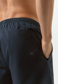 Shorts de bain bleu marine en tissu texturé, dotés d'une taille élastique et d'une poche arrière avec un petit œillet circulaire.