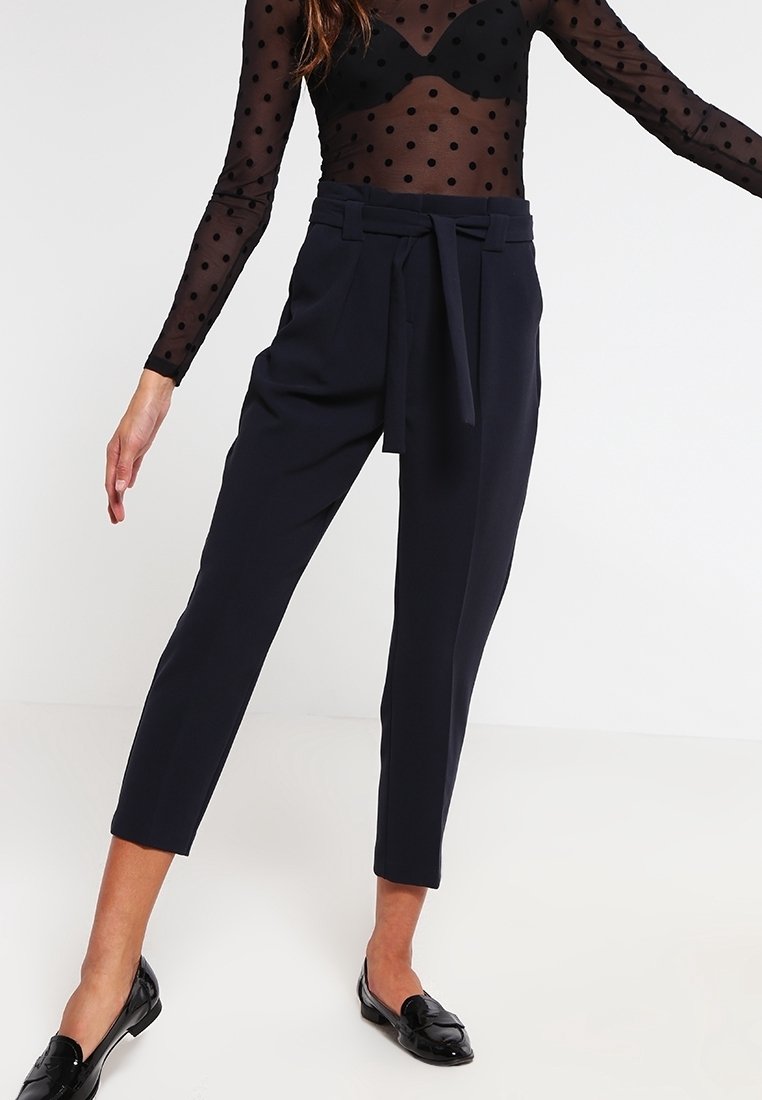 Marina skräddarsydda byxor med hög midja och knytning framtill, med smalnade ben och lätta material. Glansiga svarta loafers fulländar looken.