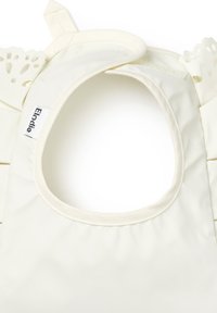 Vit tygbinda med rund halsöppning och scalloped kanter, med en Elodie-etikett. Slät textur och enkel design.
