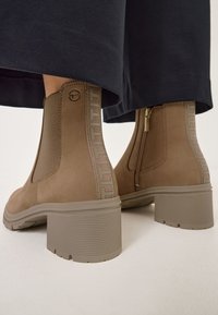 Bottines marron en daim avec un panneau latéral texturé, un talon en caoutchouc strié et une fermeture éclair sur le côté pour un enfilage facile.