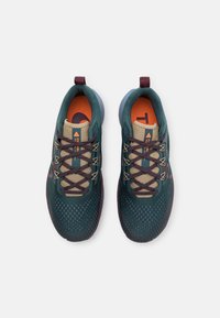 Ciemnozielone buty sportowe z teksturowaną cholewką, beżowymi sznurówkami, pomarańczowym wnętrzem oraz fioletowymi akcentami na podeszwie i pięcie.