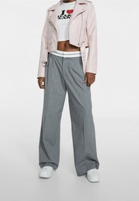 Hellrosa, verkürzte Bikerjacke, weiße Grafik-T-Shirt, graue, weit geschnittene Hose und weiße Sneakers. Glatte Textur, lockere Passform und kontrastierende Farben.