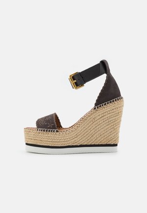 Bruine suède wedge sandaal met een enkelbandje, voorzien van een gestructureerde jute zool, witte rubberen basis en decoratieve stiksel op het bovenwerk.