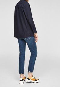 Marinblå skjorta med knapplåsdesign, blå jeans med fransade fållar och chunky sneakers med orange, svart och vitt som accentfärger.