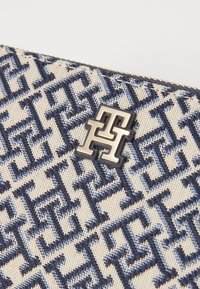Canvas clutch featuring a cream background with a repeating navy geometric pattern, accented by a metallic logo in the center.