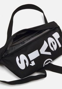 Czarna torba na suwak wykonana z trwałego materiału, z wyraźnym białym logo. Zawiera pasek na ramię do łatwego noszenia.