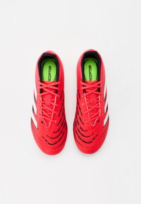 Chaussures de football rouges avec un dessus texturé, des rayures noires et blanches, et des motifs découpés complexes. Intérieur vert néon avec des lacets.