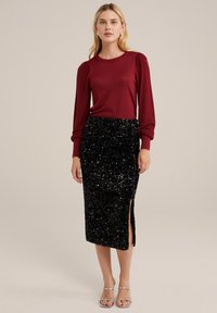 Bordo ilgomis rankovėmis megztinis, derinamas su prigludusia juoda sequin midi sijonu, turinčiu šoninius plyšius, ir atvirų pirštų sidabriniais basutėmis.