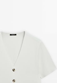 Blouse gris clair à manches courtes avec un décolleté en V et trois boutons marron. Texture lisse et design ajusté, étiqueté « Massimo Dutti ». 